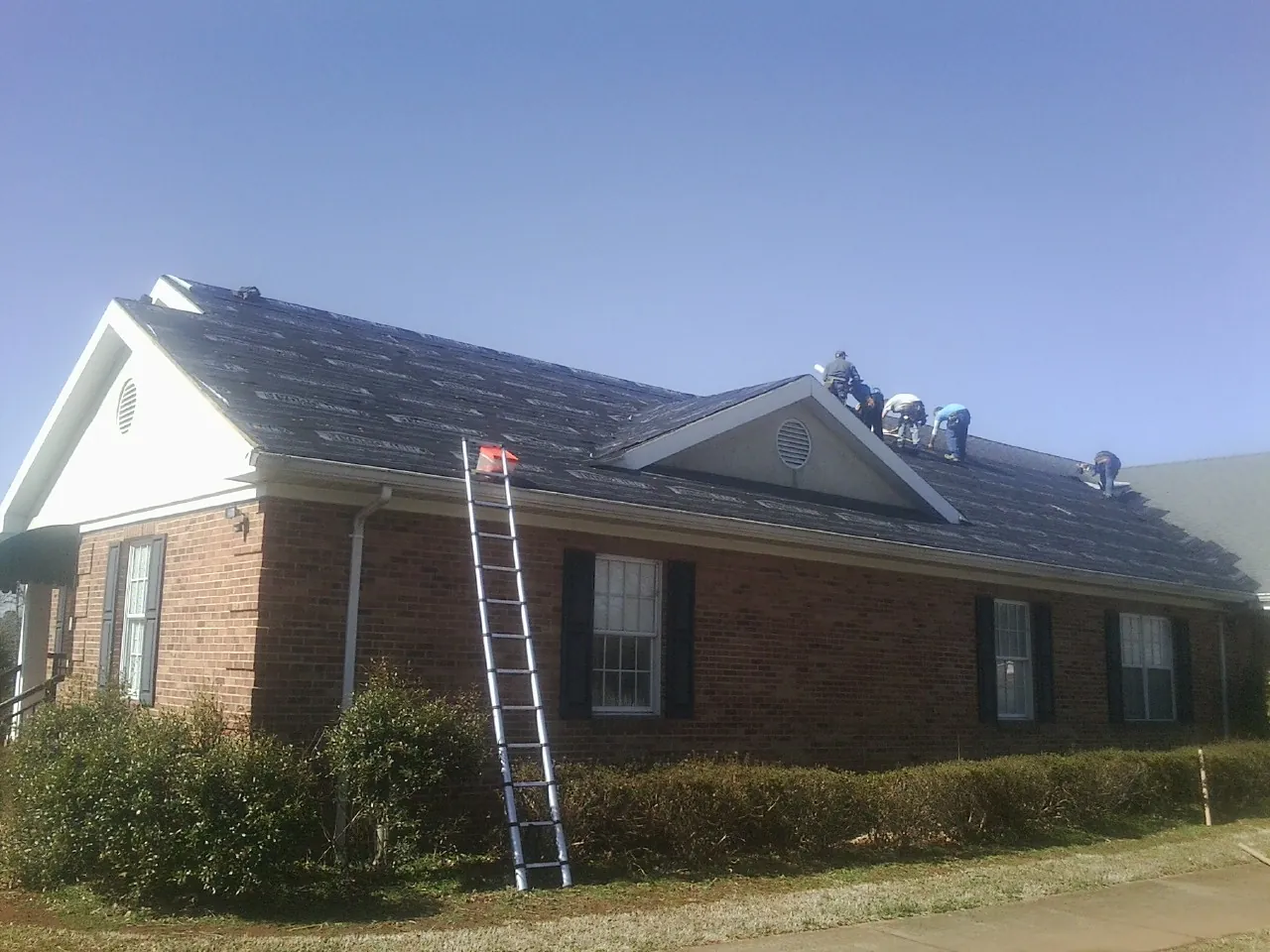 Crew tearing shingles off a brick ranch roof with a ladder set — Emergency Roof Repair work by our crew in Hartland
