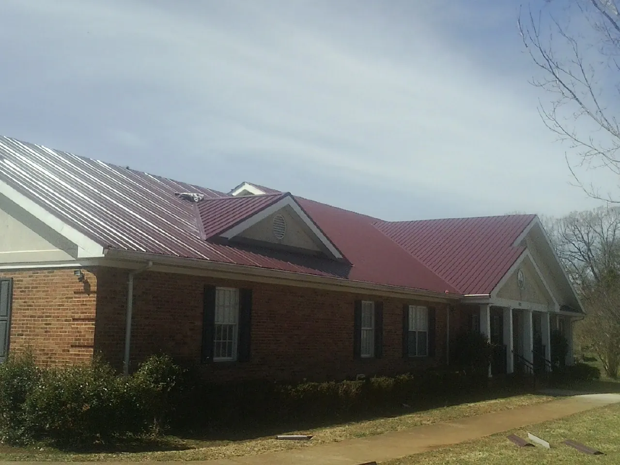 Red metal roof with gabled entries on a long brick building, from a Hail Damage Roof Repair job in Hartland