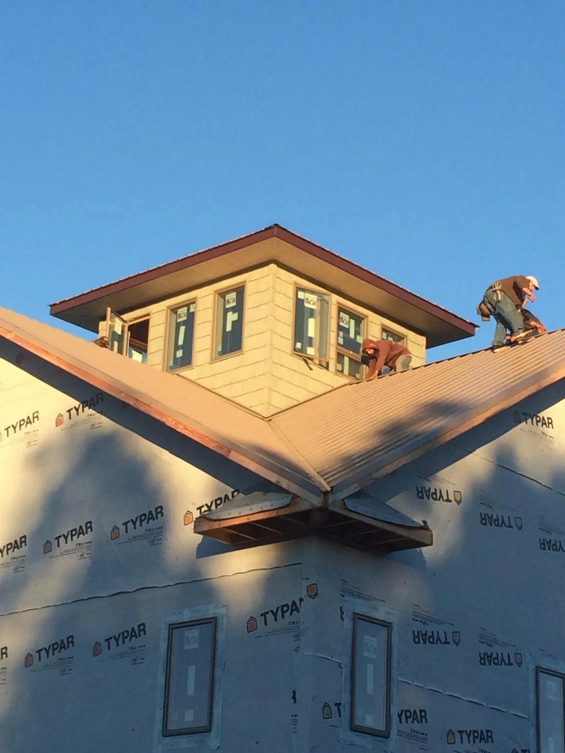 Roofers working around a rooftop cupola on a new metal roof at sunset — Roof Waterproofing in Hartland by Roofing Brothers
